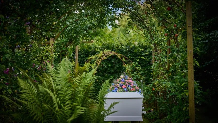 Hvid kiste med blomster i en naturskøn have – Kim Bondo Bedemand